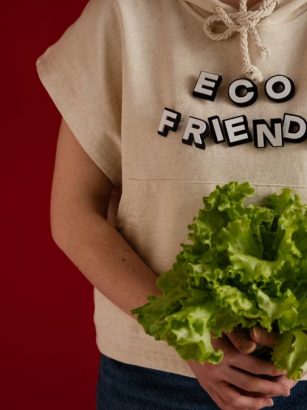 Woman in an eco-friendly hoodie holding fresh lettuce against a red background.