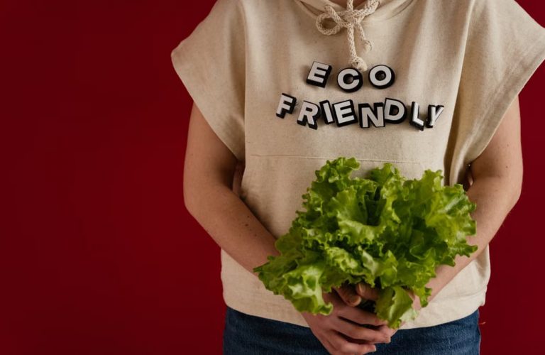Woman in an eco-friendly hoodie holding fresh lettuce against a red background.