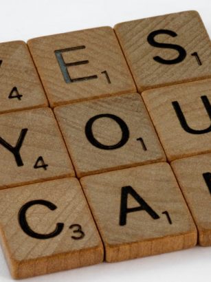 Wooden Scrabble tiles on white surface spelling 'Yes You Can,' promoting positivity and motivation.
