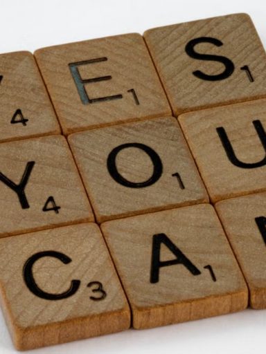 Wooden Scrabble tiles on white surface spelling 'Yes You Can,' promoting positivity and motivation.
