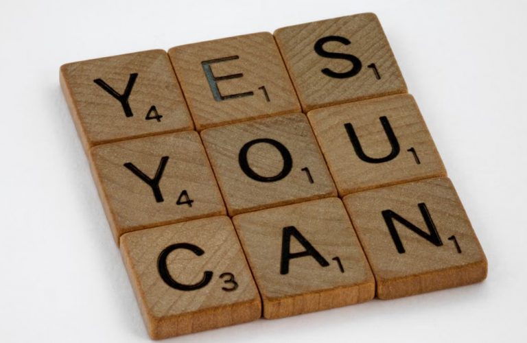 Wooden Scrabble tiles on white surface spelling 'Yes You Can,' promoting positivity and motivation.